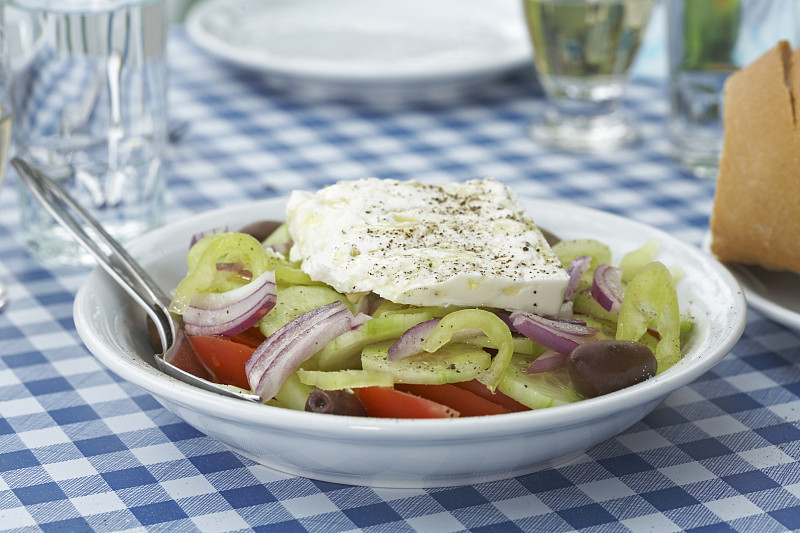 希腊沙拉在餐桌上的玻璃杯和盘子的背景。图片下载