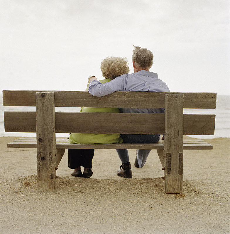 一对情侣一起坐在海滩的长椅上图片下载