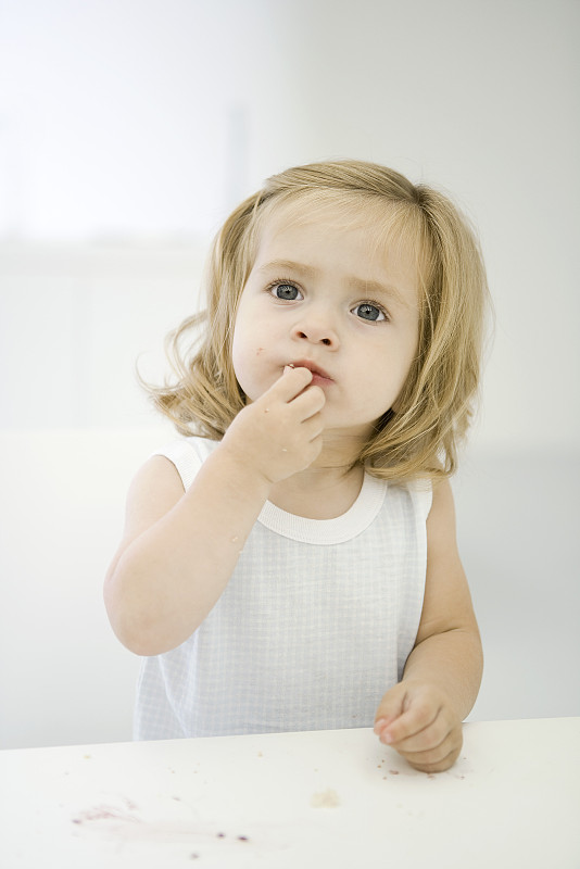 小女孩坐在凌乱的桌子旁，擦着嘴唇上的面包屑图片下载