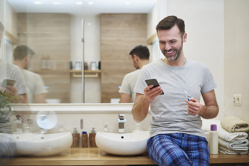 男人在浴室刷牙和使用手机。Debica、波兰图片下载