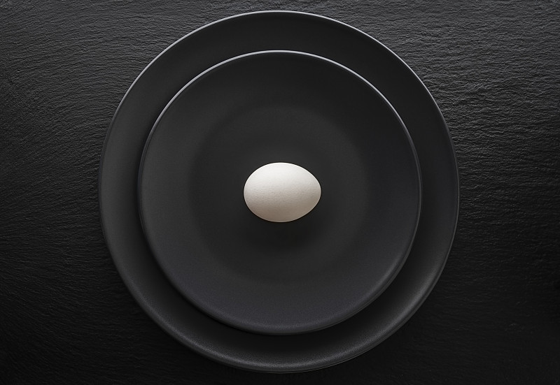 一个鸡蛋放在一个黑色的盘子里。这个盘子放在一个黑色的石板盘子上。图片素材