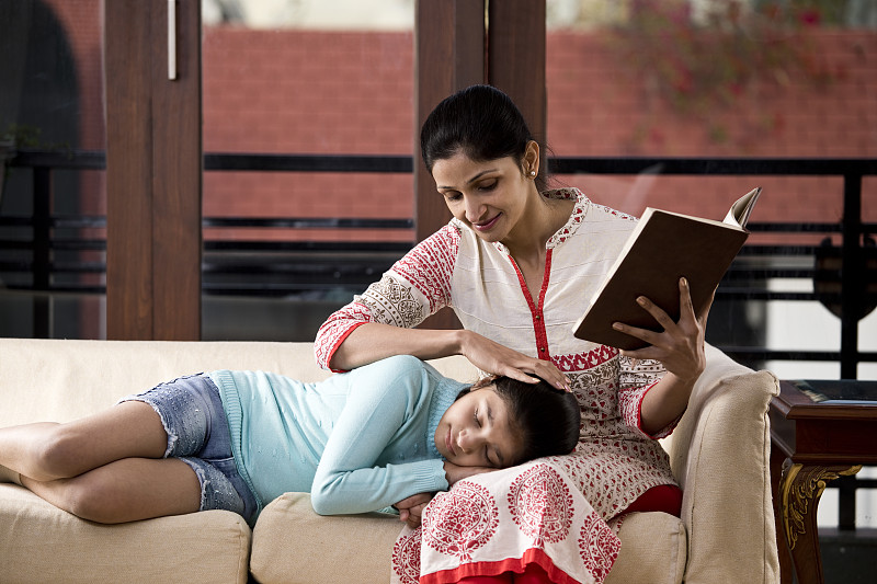 一个女人在看书，女儿睡在她的腿上图片下载