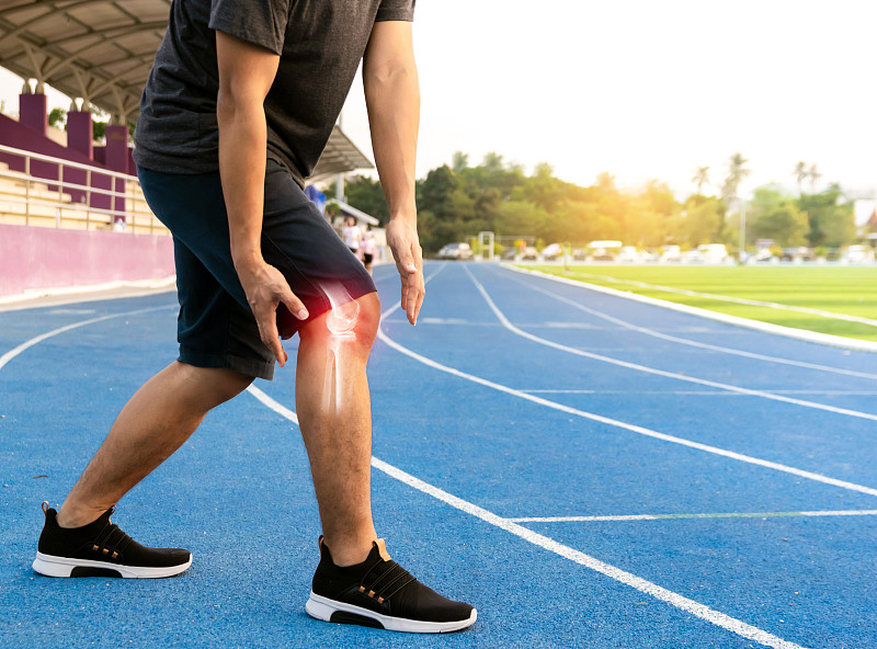 膝盖疼痛的男人站在跑道上图片素材