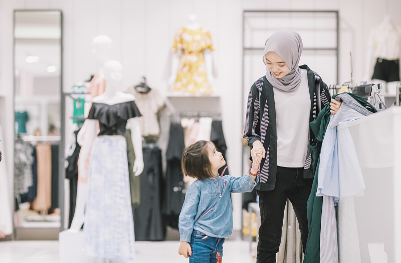 一位年轻的亚洲马来人在一家精品店购物，她的女儿在排队付款图片素材