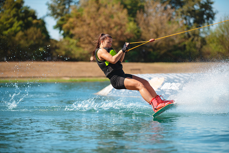 运动的年轻女子在湖上骑尾流板图片素材