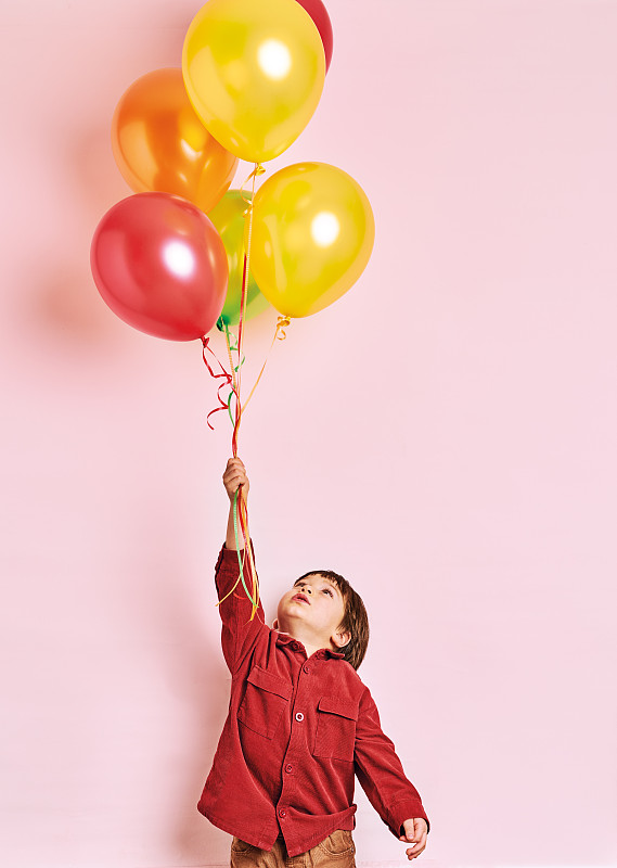 可爱的孩子拿着彩色的氦气球在粉红色的背景。他是快乐的。图片下载