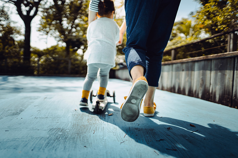 后视图年轻的亚洲母亲教她可爱的小女儿在公园骑滑板车。他们在一起享受美好时光图片下载