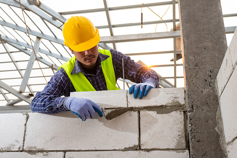砌砖工人使用蒸压加气混凝土砌块。筑墙，在建筑现场安装砖块，工程和建筑概念。图片素材