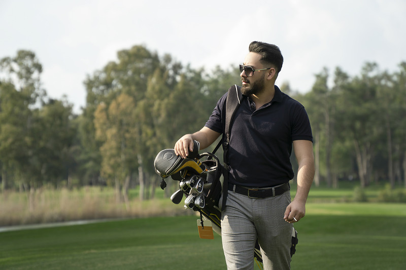 帅气的年轻高尔夫球手的肖像携带着高尔夫球袋在高尔夫球场图片下载