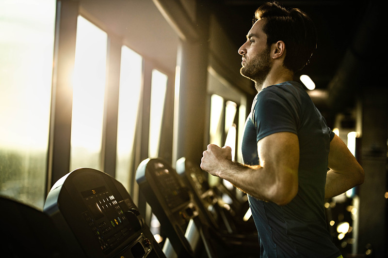 积极的男性运动员在健身房的跑步机上慢跑。图片下载