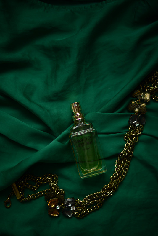绿色背景上的香水瓶和项链图片素材