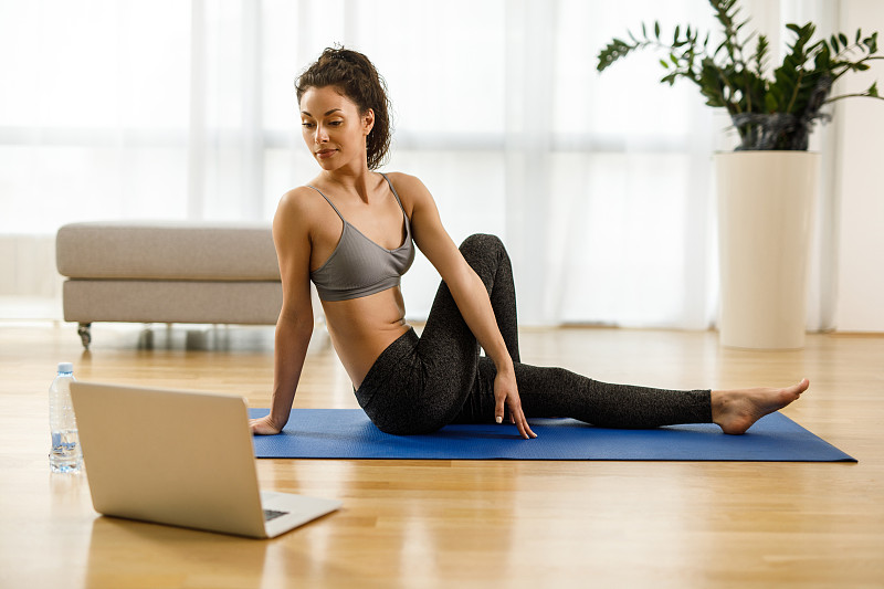 穿着运动服的女人一边练瑜伽，一边在笔记本电脑上看辅导课图片下载