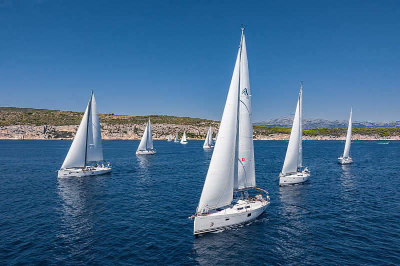 航拍的游艇比赛，一场帆船赛，激烈的竞争，很多白色的帆，岛上是背景，顶级旅游目的地，度假在克罗地亚，田园诗般的风景图片下载