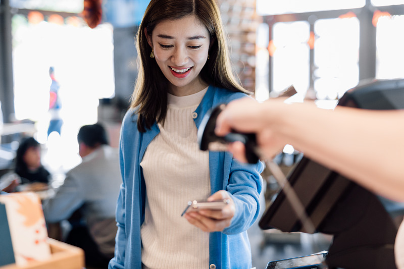 一名亚洲年轻女子在咖啡馆用智能手机付款。图片下载