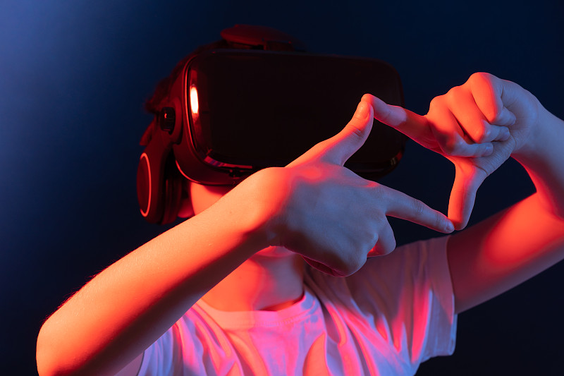戴着虚拟现实眼镜的男孩。霓虹灯。远程学习。带虚拟现实眼镜的3d游戏。图片下载