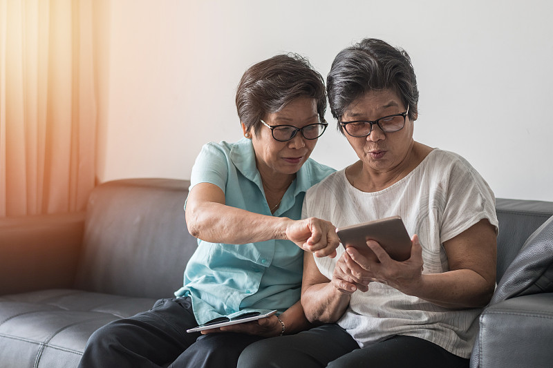 老年社会理念，亚洲老年女性姐妹利用手机数字平板智能手机应用社交媒体网络，通过互联网在朋友圈交流图片下载