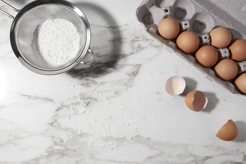 用面粉、鸡蛋纸盒和面粉筛在大理石表面上烘烤配料图片下载