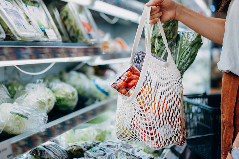 年轻的亚洲妇女在超市购买新鲜的有机食品杂货的镜头。她正用一个棉网环保袋购物，里面装着各种水果和蔬菜。“零浪费”的概念图片下载
