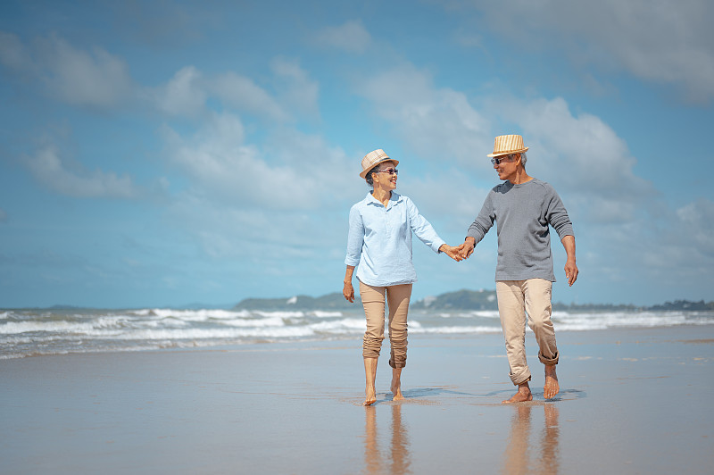 一对老年夫妇在海滩上牵手散步图片下载