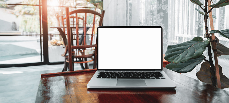 笔记本电脑空白白屏幕上的桌子在咖啡馆的背景。笔记本电脑与空白屏幕上的咖啡店模糊背景。图片下载