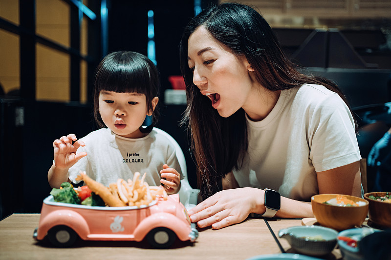 可爱的亚洲小女孩与她的母亲在餐厅用餐。当孩子们的饭菜被端上餐桌时，他们看起来很兴奋，迫不及待地开始吃了图片素材