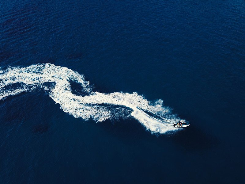 一艘喷气式快艇在深蓝色的海水中打旋的鸟瞰图。船的尾流从上面。图片下载