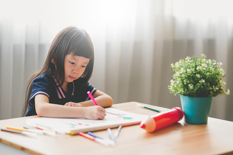 甜美的亚洲小女孩坐在桌子上，用彩笔在客厅画画图片下载