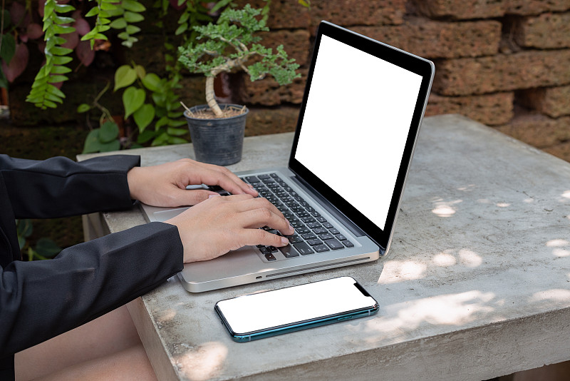 一位在户外花园使用笔记本电脑的亚洲女性。图片素材