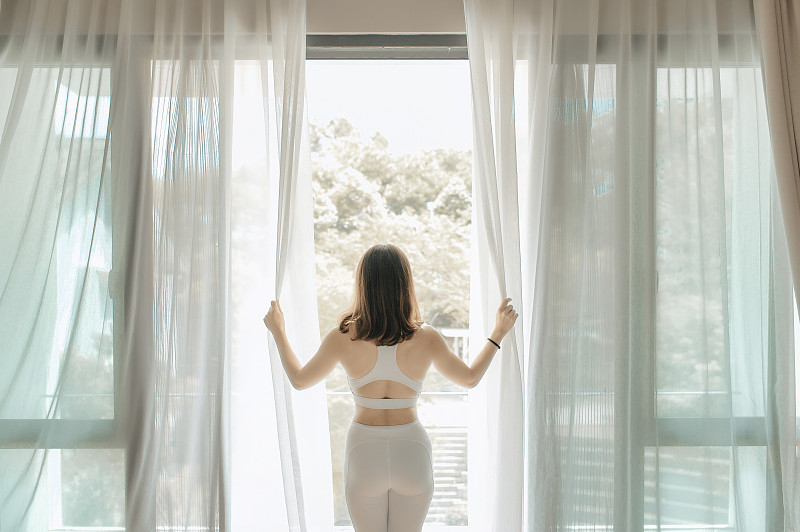早上，一位亚洲的中国美女拉开窗帘，走到阳台上，准备练瑜伽图片下载