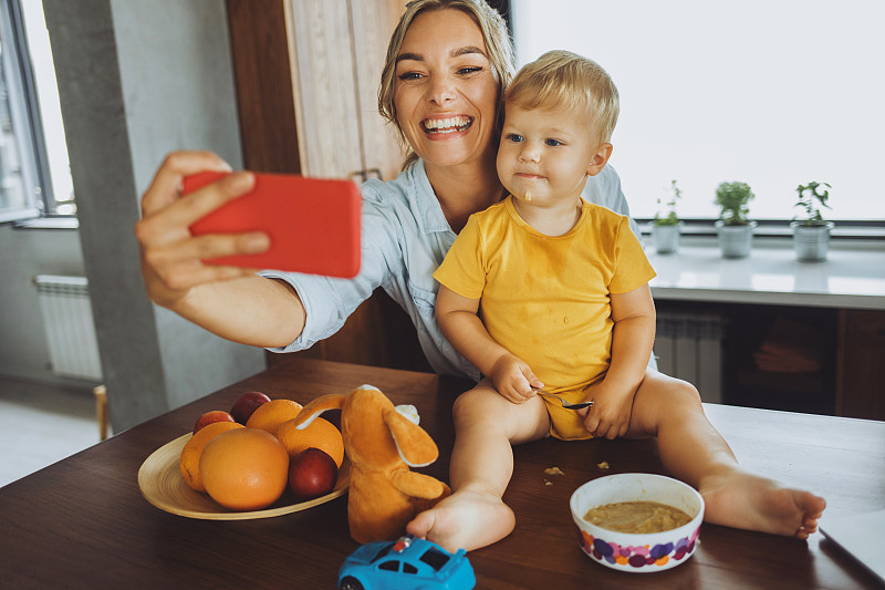 千禧一代的妈妈在用智能手机和男婴自拍图片下载
