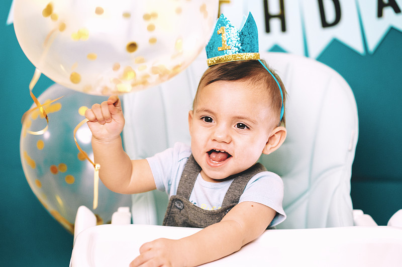 在生日聚会上，可爱的小男孩在高椅子上拿着气球图片素材