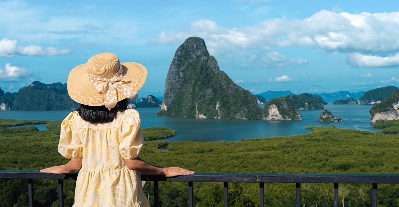 身穿黄色连衣裙的女子站在泰国攀雅同廊社岛的视点看阳光下的山。图片下载