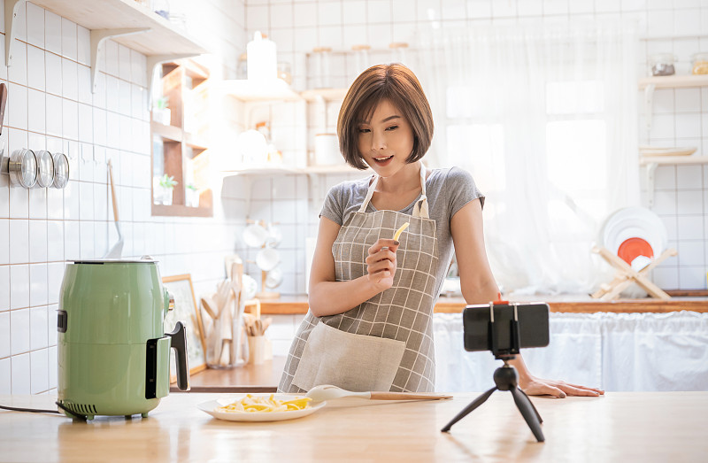 美丽的亚洲女人的肖像评论烹饪土豆食物，用空中飞行智能设备在家里录制直播视频。网红女孩对社交媒体营销、爱好和休闲概念的理解图片素材