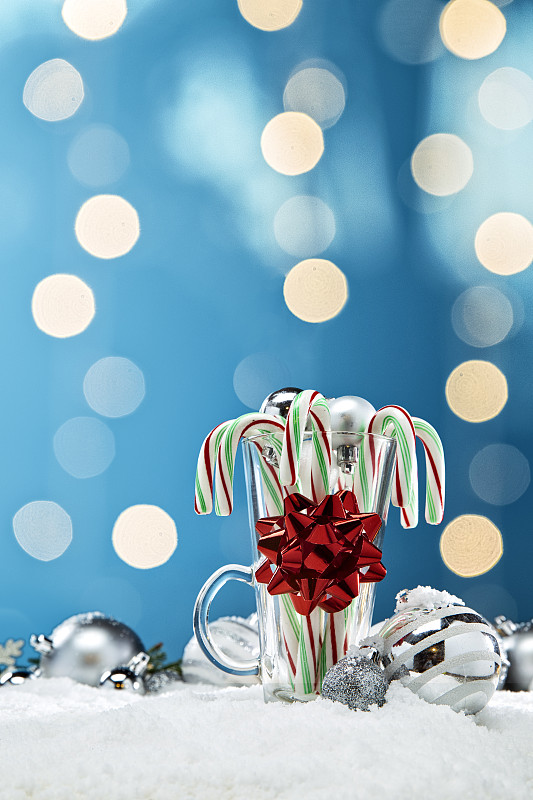 玻璃糖果拐杖周围的蓝色和白色圣诞装饰品和灯在雪与松树树枝图片下载