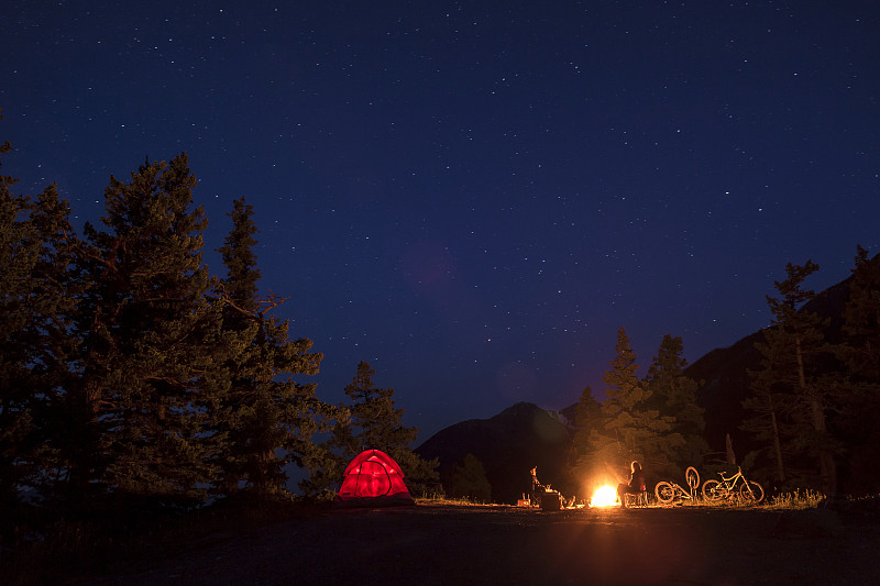 夫妇坐在火后山地自行车，露营野外。图片下载