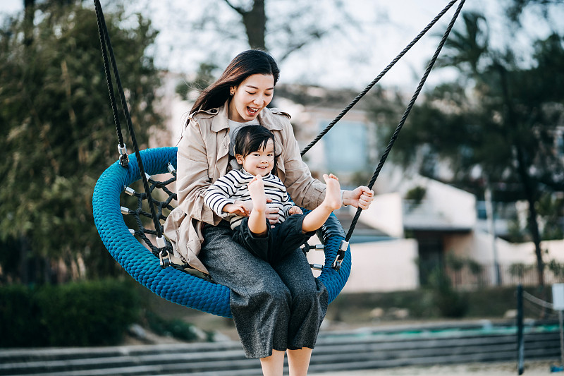 可爱的亚洲小女孩坐在她妈妈的腿上，在公园的篮子秋千上玩得很开心。快乐地微笑，享受高质量的母女家庭团聚时光图片下载