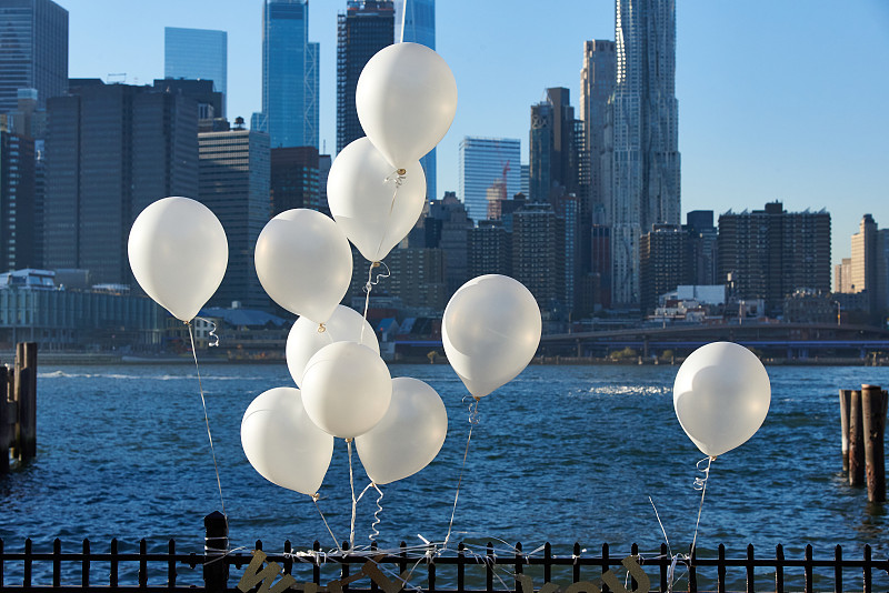 布鲁克林大桥公园的栏杆上系着白色气球。后面是东河和曼哈顿下城的天际线图片下载