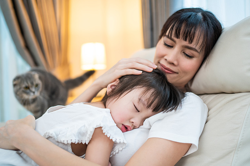 亚洲美丽慈爱的母亲拥抱熟睡的女婴在她的臂弯温柔。父母抱着小婴儿靠在肩上，和小女儿一起睡觉。家庭亲子关系概念。图片下载