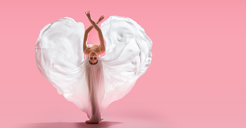 优雅的芭蕾舞女演员穿着尖头鞋，穿着白色长裙在粉红色的背景上显现出心形图片下载