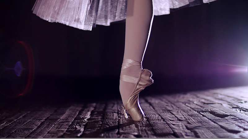 在聚光灯下，老剧院舞台上的特写。芭蕾舞女演员身穿白色芭蕾舞裙，穿着尖头鞋踮着脚尖旋转，优雅地表演一定的芭蕾舞动作、舞姿、足尖图片下载
