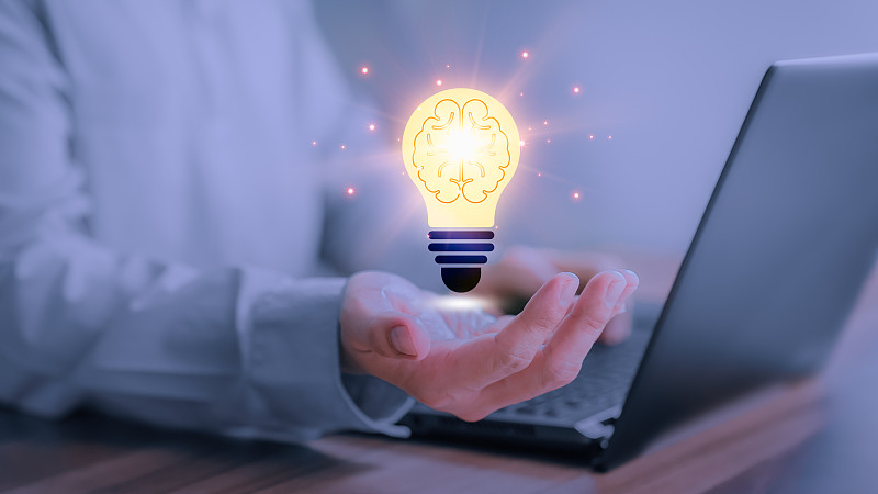 男人拿着一个抽象的灯泡在电脑前工作，用技术创新和创造力思考和创造新的想法，灵感来自在线技术，创新。图片下载