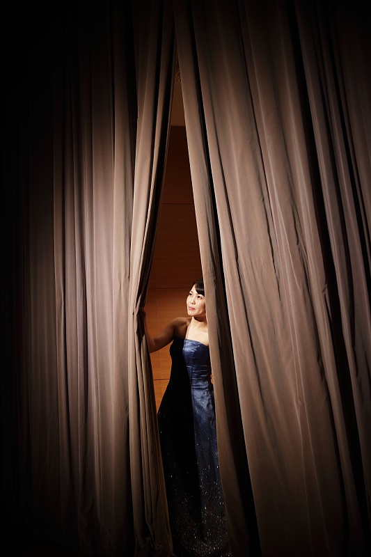 从音乐厅舞台的窗帘中窥视的女性图片素材