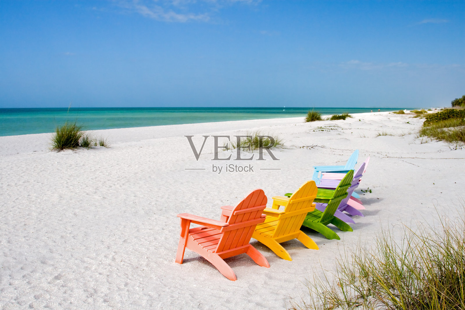 六把彩色的椅子放在空荡荡的海滩上，面向大海照片摄影图片