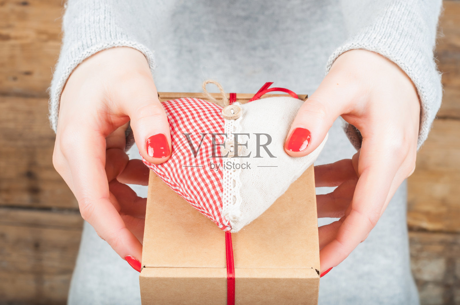 手握礼物在牛皮纸盒上的木制背景。情人节的概念，婚礼，订婚，母亲节，生日，新年，圣诞节，节假日。照片摄影图片