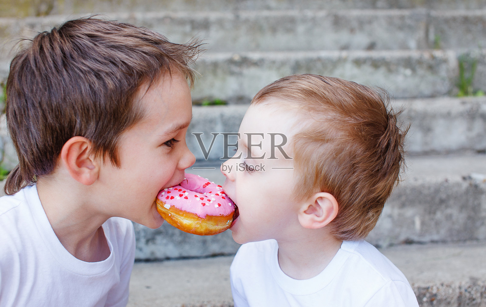 两个孩子咬下一个甜甜圈，玩得很开心照片摄影图片