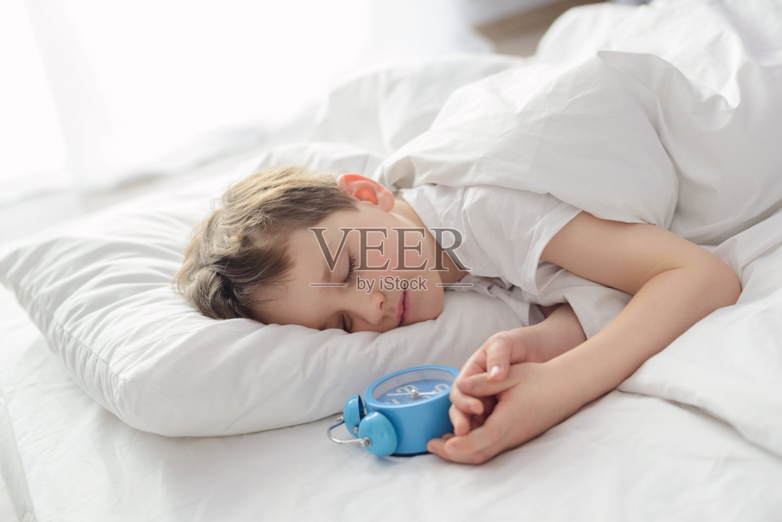 小男孩睡在白色的床和闹钟照片摄影图片