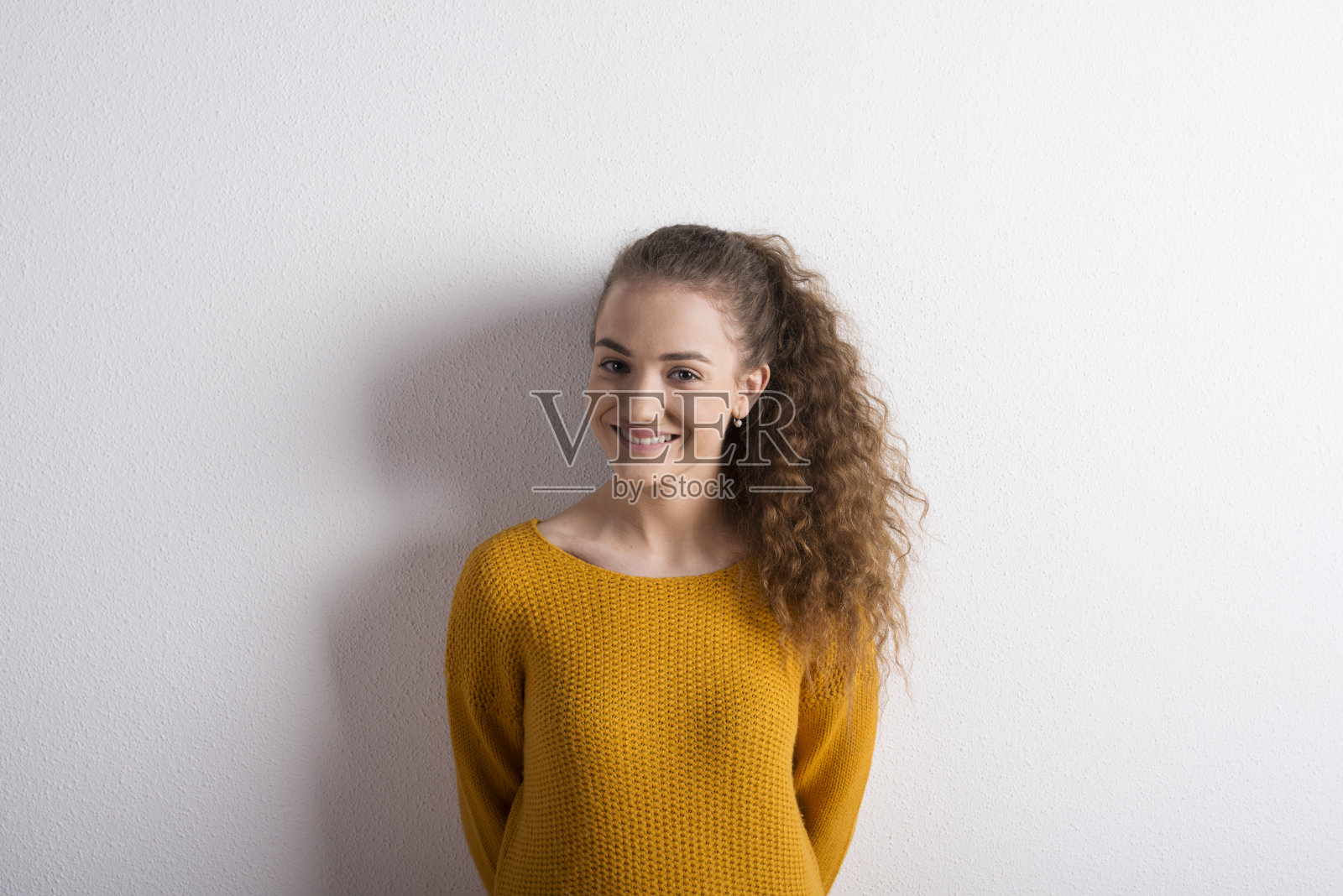 卷发女孩穿着黄色毛衣，在摄影棚拍摄。照片摄影图片