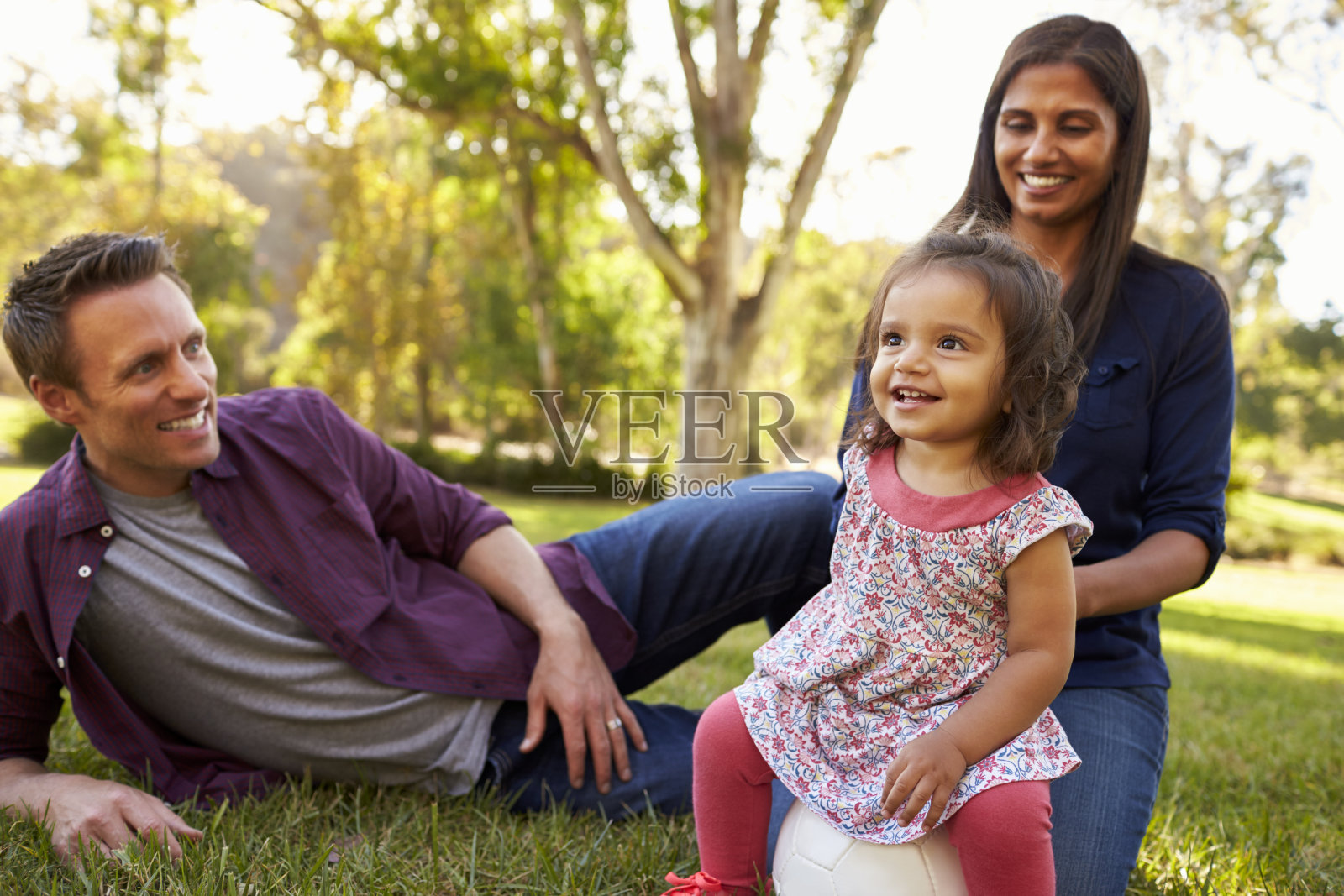 混血儿父母和小女儿坐在公园里，照片摄影图片