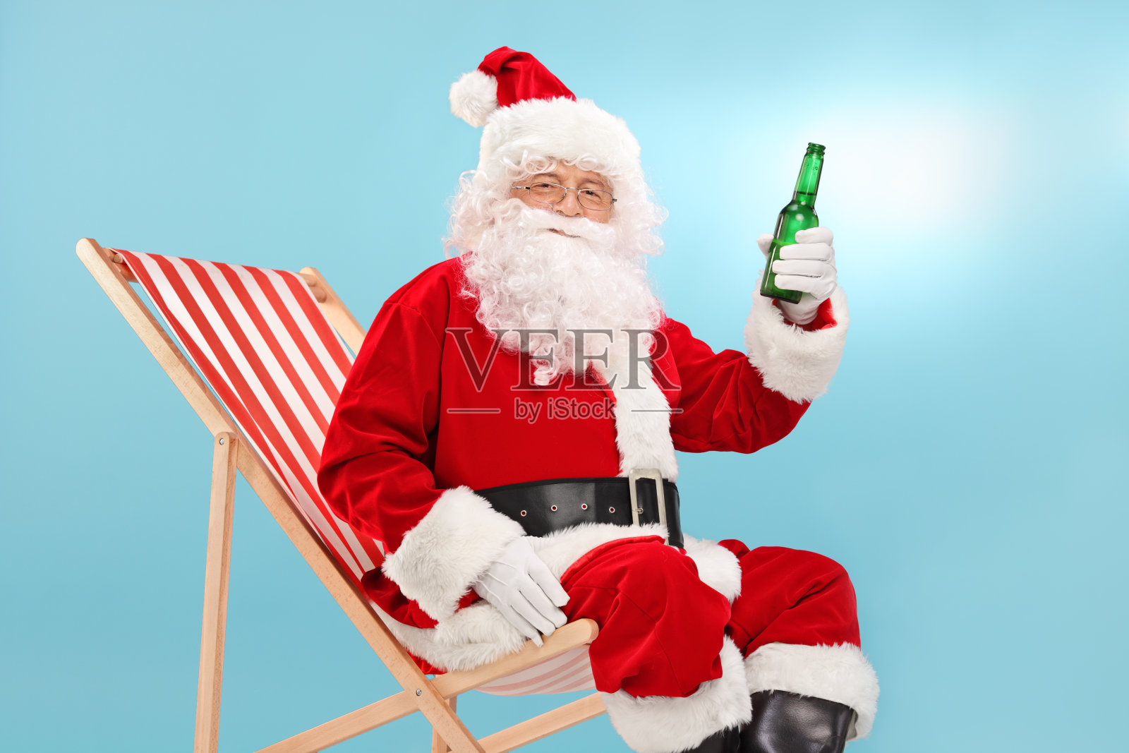 圣诞老人拿着啤酒坐在阳光躺椅上照片摄影图片