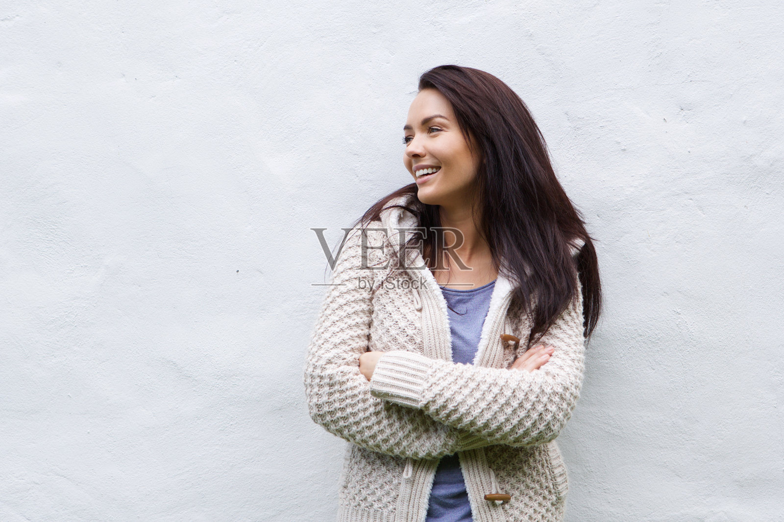 穿着羊毛衫的微笑女人靠着白色的墙站着照片摄影图片